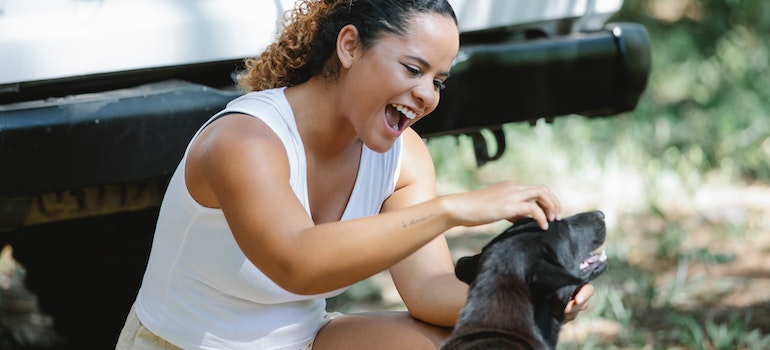 A woman petting her dog next to the car.